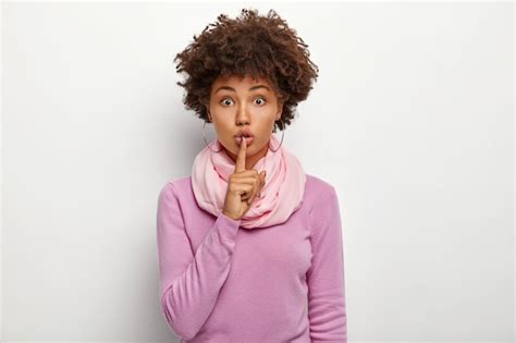 free photo pretty curly haired woman holds index finger over lips