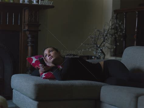 middle aged woman lying on sofa watching tv at night holding tv picture
