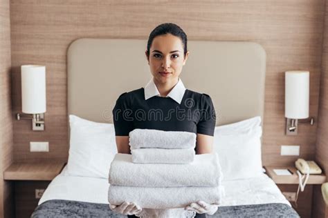 View Of Maid Holding Pile Of Folded Towels Near Bed And Looking At