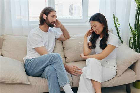 A Man And A Woman Of Different Races Sit On The Couch In A Room At Home