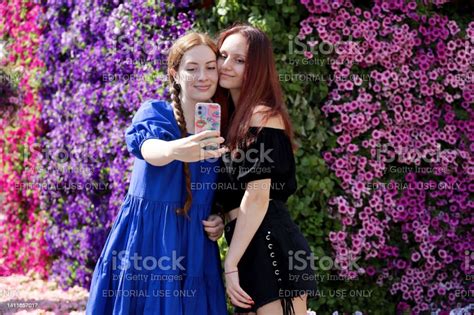 Two Girls Taking Selfie On Smartphone Camera Standing On Flower Wall