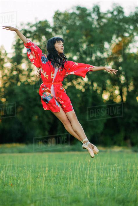 japanese ballerina in red kimono jumps on lawn and trees background