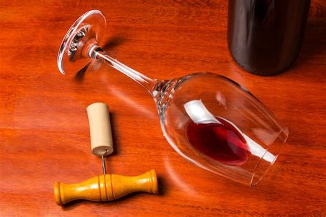 een omgevallen glas wijn met een beetje rode wijn naast een kurkentrekker en een fles op een