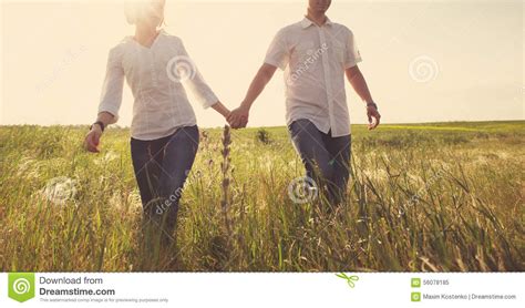 Happy Couple Holding Hands Walking Through A Meadow Stock