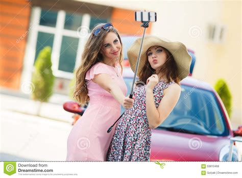 two cute girlfriends taking selfies near the car stock