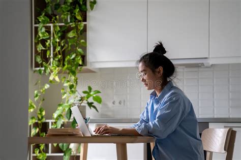 Focused Asian Woman Freelancer Working Remotely Sits At Table With