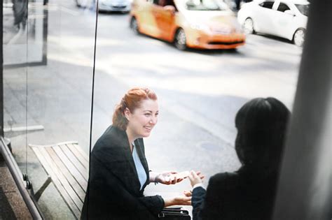 Side View Of Two Businesswomen Chatting At Bus Stop Waiting For Taxi