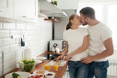 Romantic Young Couple Kissing In Kitchen While Cooking Breakfast