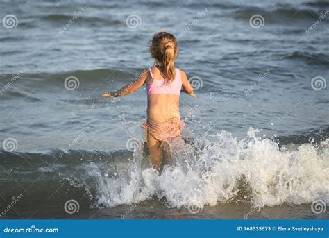 meisje  een roze badpak op het strand en kijkend naar de ochtendzee met golven stock