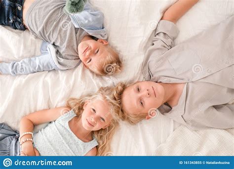 drie vrolijke blonde kinderen liggen samen op bed kijken naar camera en glimlachen twee jongens