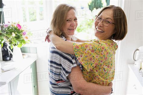 Portrait Affectionate Senior Lesbian Couple Hugging In Kitchen Stock