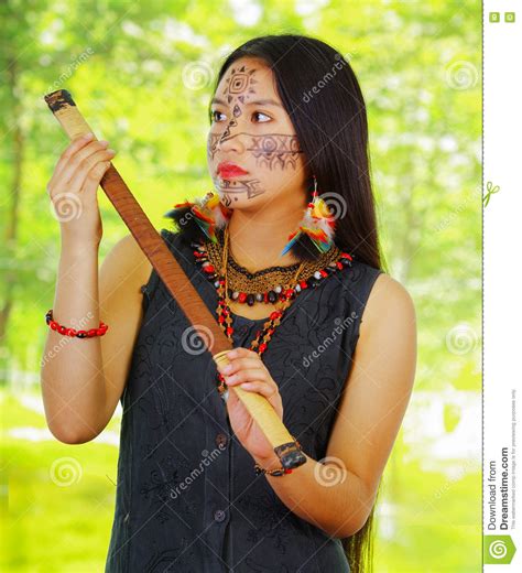 exotische vrouw uit de amazone met gezichtsverf en zwarte kleding die blaaspijp bosachtergrond