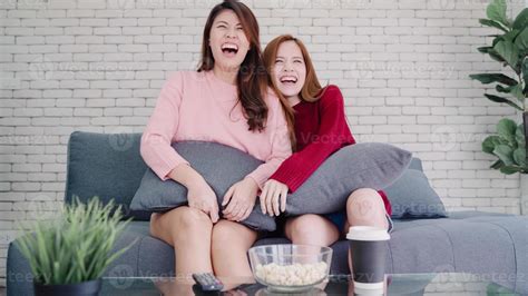 Lesbian Asian Couple Watching Tv Laugh And Eating Popcorn In Living