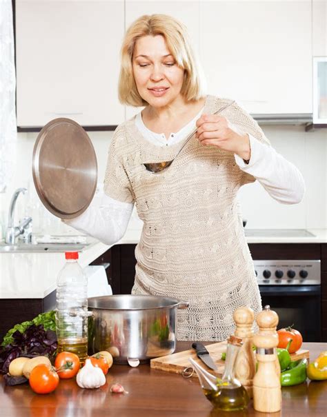 happy mature housewife with ladle cooking soup in pan in kitchen stock