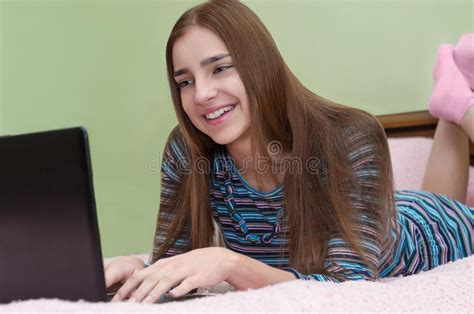 mulher de sorriso bonita nova que usa o laptop que encontra se na cama