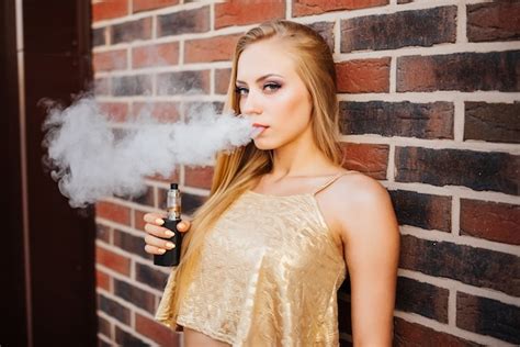 Vaping 야외에서 연기와 전자 담배를 흡연하는 젊은 아름 다운 여자 증기 개념 무료 사진
