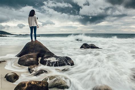 woman standing on a rock looking out to a stormy sea stocksy united