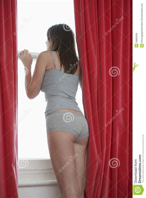Woman In Nightwear Looking Out Through Window At Home