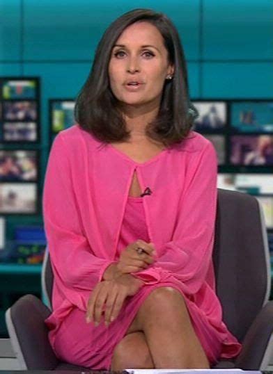 A Woman In A Pink Dress Is Sitting On A News Desk And Looking Off To