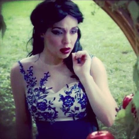A Woman In A Blue And White Dress Holding An Apple While Looking At The