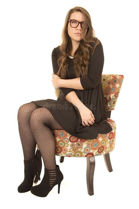 coy female model wearing black dress and glasses sitting down stock