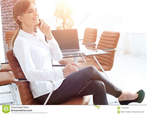 jonge vrouwelijke medewerker die op telefoonzitting dichtbij de desktop spreken stock foto