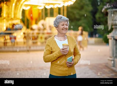 Pretty Granny With Cup Of Coffee Using Mobile Phone In Summer Park
