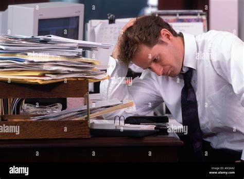 stressed male office worker sitting  desk  piles  papers stock