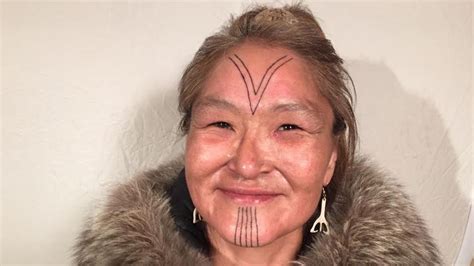 An Older Woman With Tattoos On Her Face And Eyebrows Smiles At The