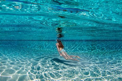 teenage girl floating underwater in a large deep blue swimming pool