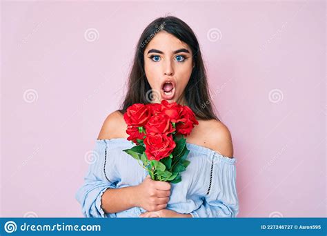 Brunette Teenager Girl Holding Flowers Afraid And Shocked With Surprise