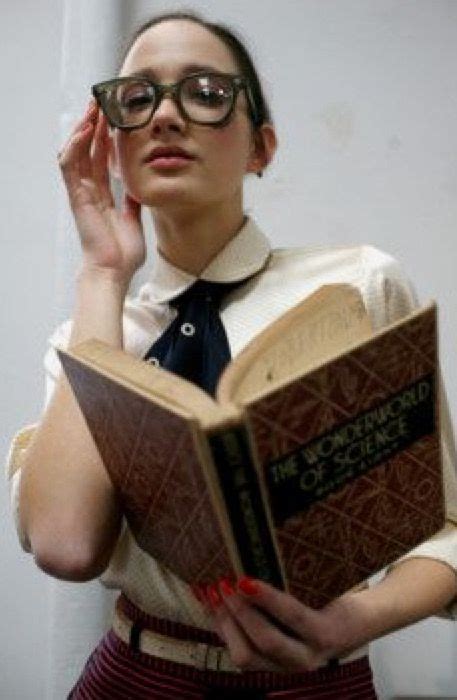 a woman wearing glasses and holding an open book in her right hand