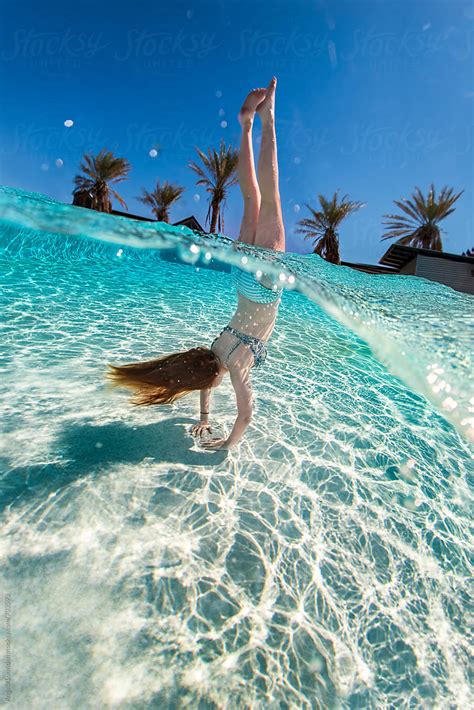 girl in a bikini doing a handstand in a swimming pool with an over