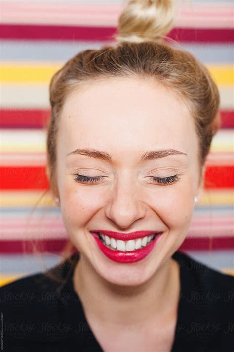 woman with red lips laughing in front of a striped wall by stocksy