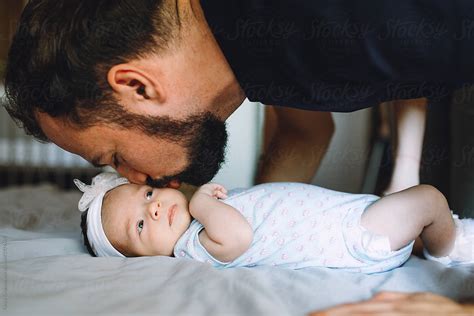 father kissing his newborn daughter by stocksy contributor tanya