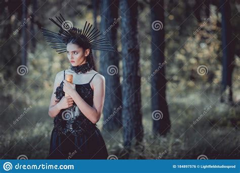 Woman In Witch Costume Standing On Forest Background Looking Away