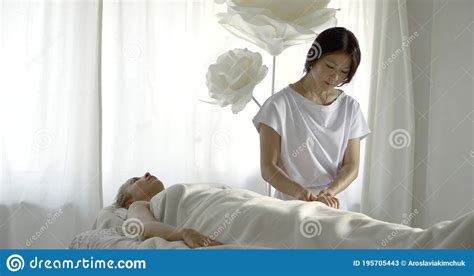 asian masseuse is stroking fingers arm and head of relaxed female