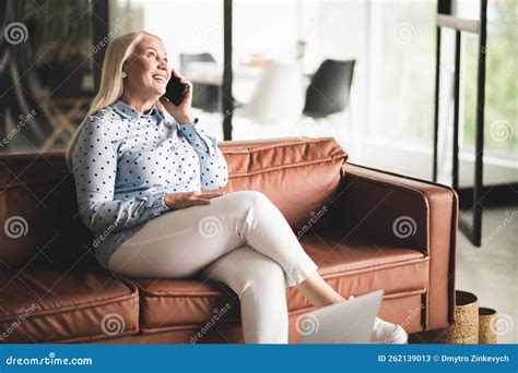 Blonde Mature Woman Talking On The Phone While Sitting On The Sofa