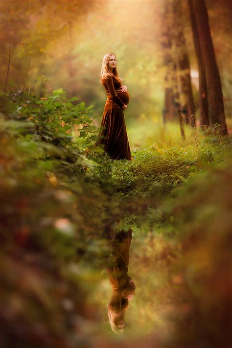 foto van een zwangere vrouw die  het water staat  een herfstbos  een mooie jurk voor een