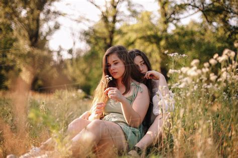 Thoughtful Lesbian Couple Sitting In Field Of Flowers In Forest Stock