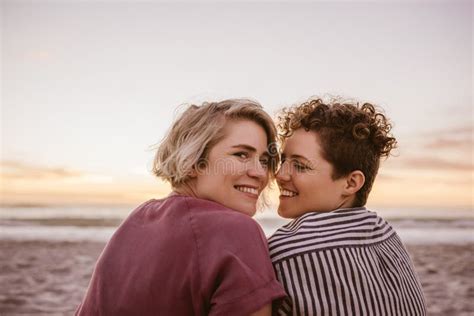 Smiling Young Lesbian Couple Watching A Beach Sunset Together Stock