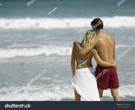 a couple standing on the beach with their arms around each other stock