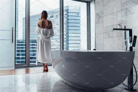 Back View Of Young Woman Wearing White Bathrobe Standing In Bathroom