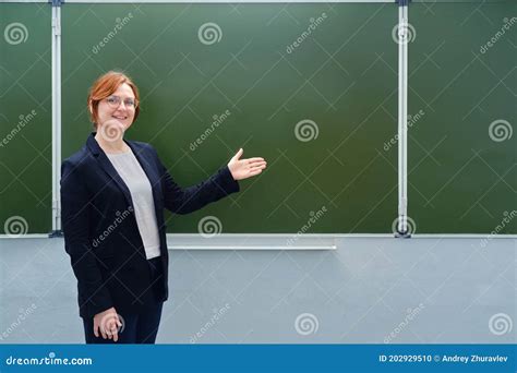 Happy Female Teacher Smiles Next To An Empty Blackboard Copy Space For