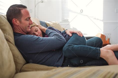 Father Sitting On A Sofa Holding His Sleepy Daughter On