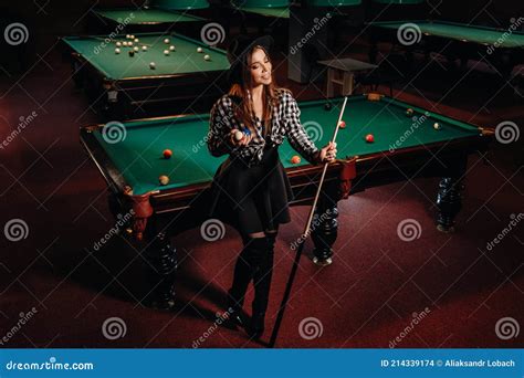 a girl in a hat in a billiard club with a cue in her hands pool game