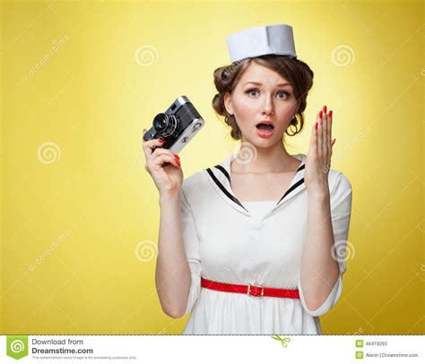 beautiful pin up girl dressed a sailor holding a vintage camera and screams behind his hand
