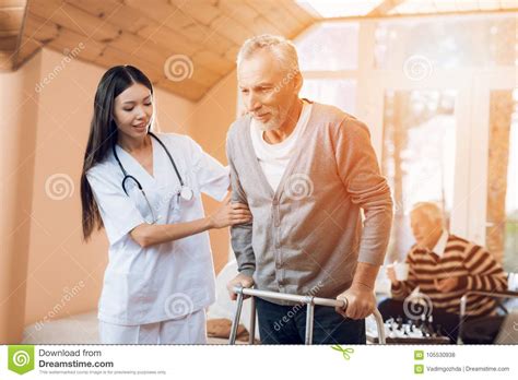 an asian nurse helps a man on an adult walker in a nursing