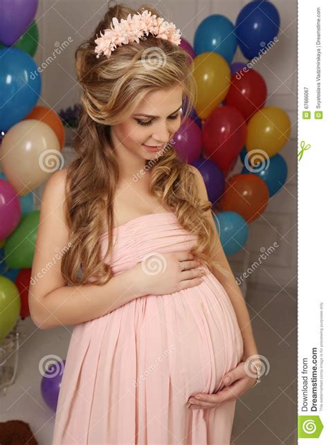pregnant woman with long blond hair in elegant dress with a lot of colorful air balloons stock