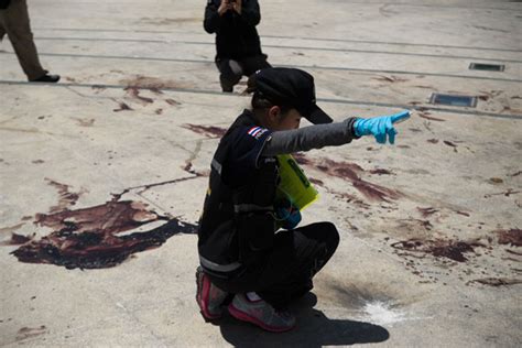 a thai forensic police officer points in the direction of where gun shots were fired next to a